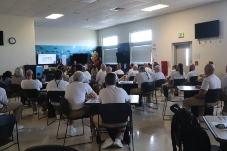 people sitting in chairs looking toward the front of the room at a person speaking